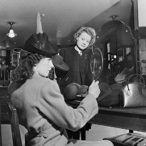 Let's Talk About Class - A customer tries on a new hat, watched by a shop assistant, in the millinery department of Bourne and Hollingsworth on London's Oxford Street in 1942 - via Wikimedia Commons.