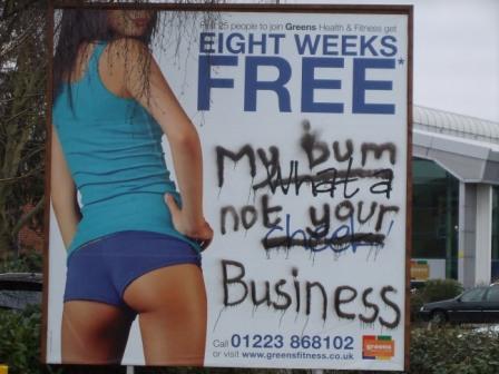 Fitness gym ad showing slim model in short shorts. Spraypaint on: "My bum not your business"