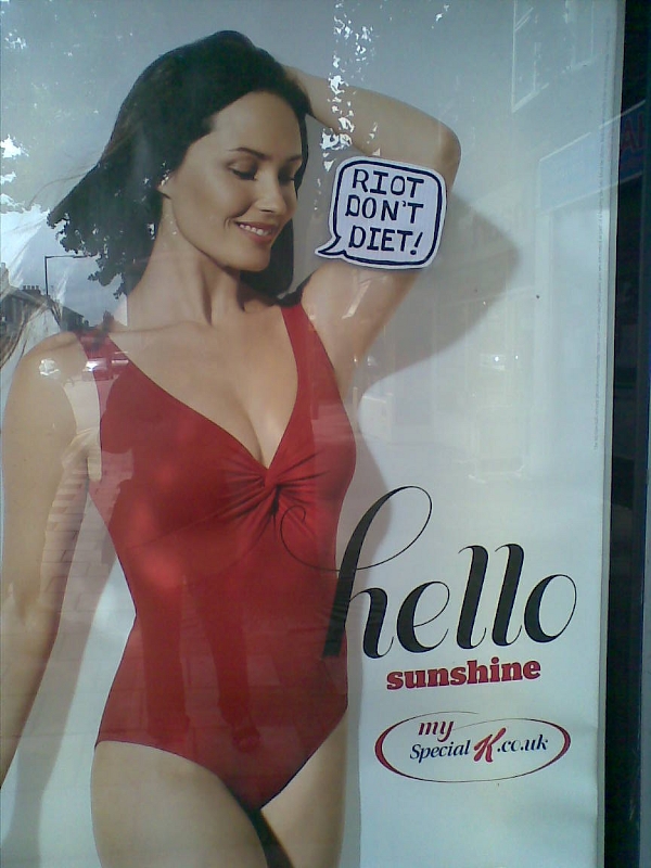 An advert for Special-K featuring a model in a red swimsuit. Someone has added a speech bubble reading 'Riot Don't Diet'