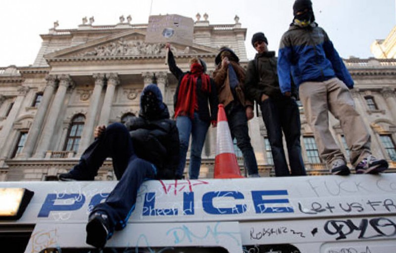 Picture of demonstrators stood on top of a graffiti-ed police van