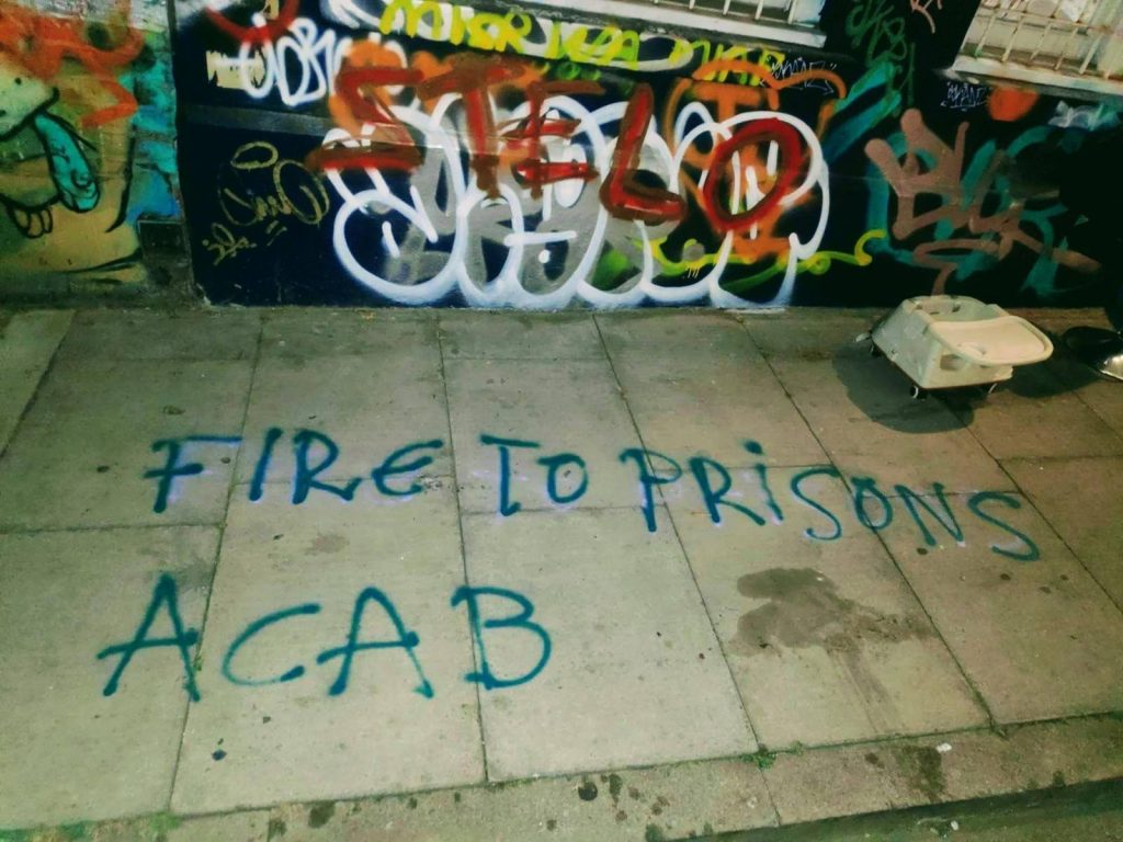 Photo of a sidewalk with the text "Fire to Prisons / ACAB" spray painted on it