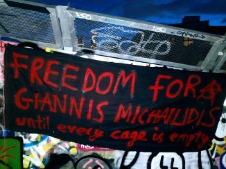 Photo of a banner hanging out in a wall full of gaffiti. The banner says “freedom for Yannis Michaelides until every cage is empty”