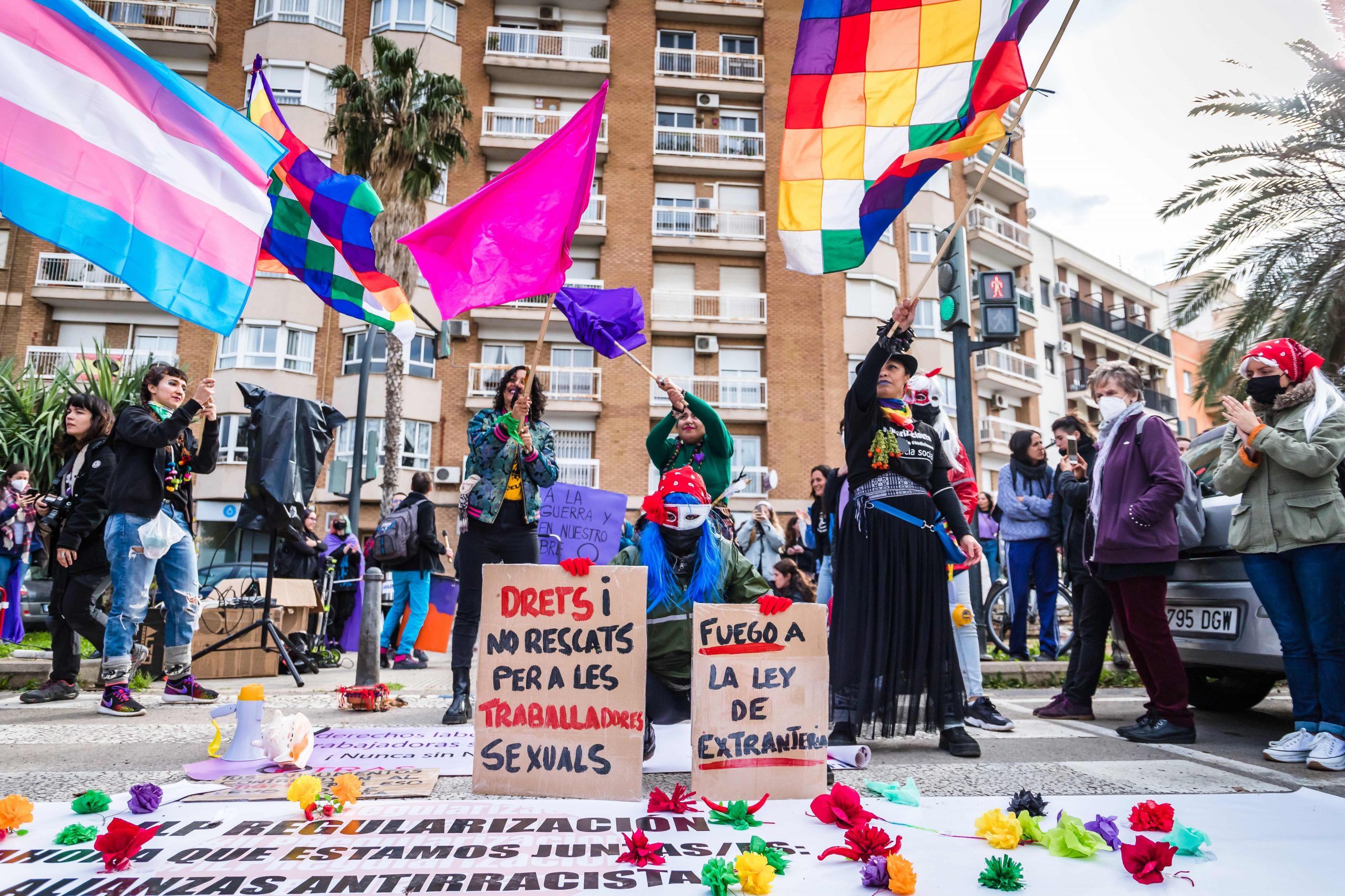 Tomada el 8M 2022, aparecen varias personas sujetando banderas incluyendo trans y wiphala (indígena), junto a varias pancartas pro-derechos y contra la Ley de Extranjería